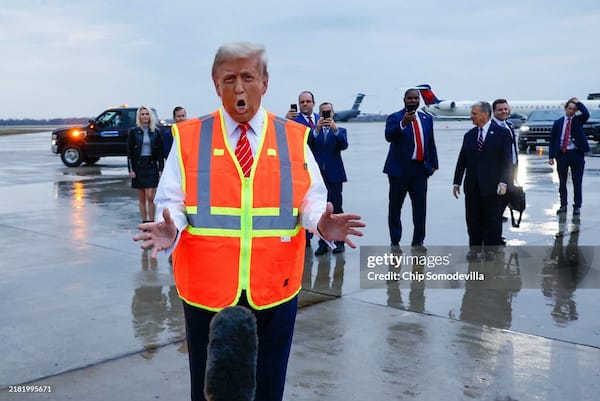 Donald Trump in an orange safety vest, clearly wearing far too much spray tan or some other kind of orange makeup on his face.