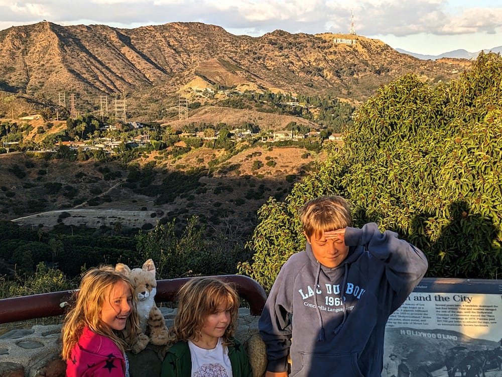 Three kids at a scenic overlook in Los Angeles with the Hollywood sign in the background.