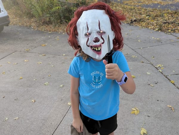 An 8-year-old child wearing a scary clown mask with glowing eyes, holding a toy knife.