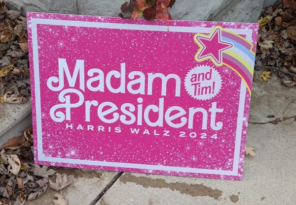 A pink Harris-Walz 2024 campaign sign reading "Madam President (and Tim!)"